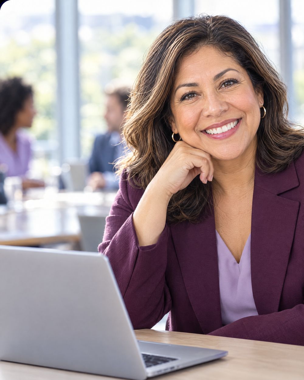 A dean in a plum blazer smiles at the camera beside her laptop.