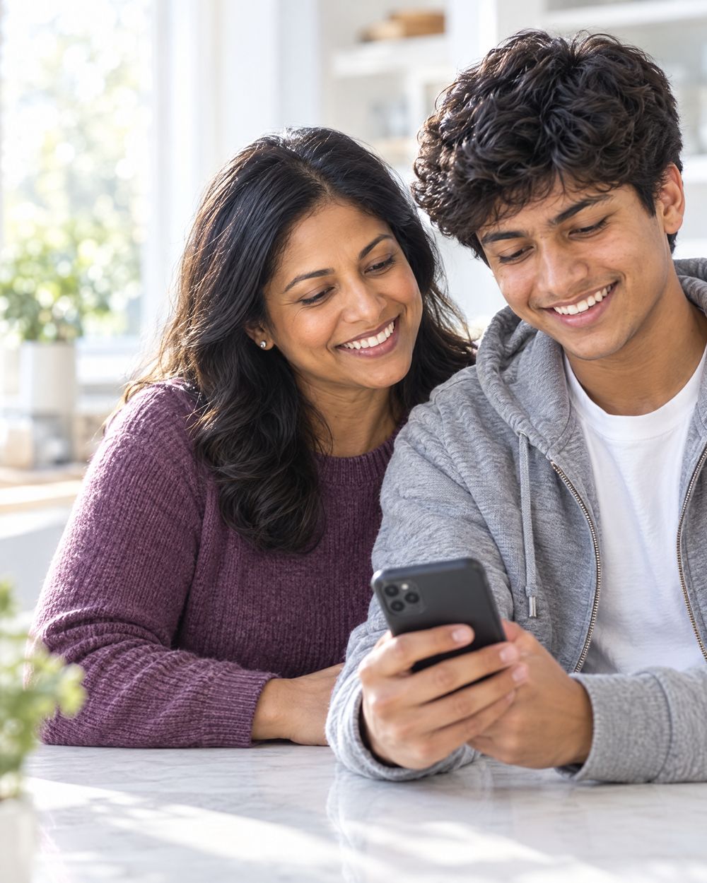 A teenage student shows a parent programs on his phone at a bright table.